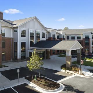 A modern residential building with a covered entrance and landscaped surroundings on a sunny day.