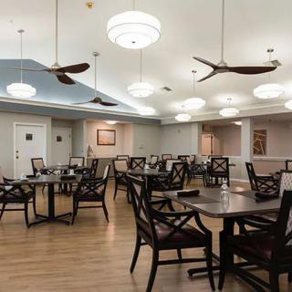 A well-lit dining area with wooden tables and chairs, ceiling fans, and a modern decor.