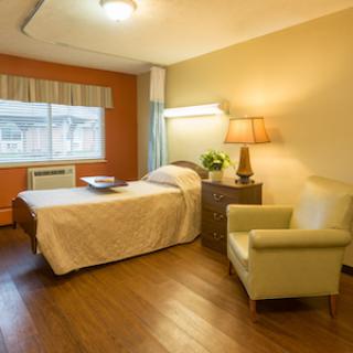 A cozy hospital room featuring a single bed, comfortable armchair, and warm lighting.