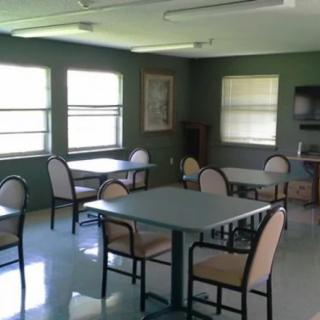 An empty dining room with tables and chairs, illuminated by natural light from the windows.