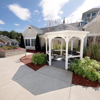 A charming white gazebo surrounded by lush greenery and a well-maintained garden pathway under a partly cloudy sky.