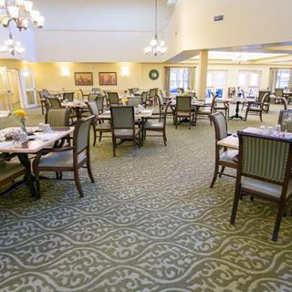 A spacious dining room with neatly arranged tables and chairs, featuring elegant lighting and patterned carpet.