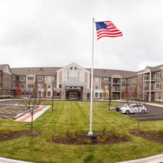 A large building with an American flag in front, featuring a neatly maintained lawn and parking area on a cloudy day.