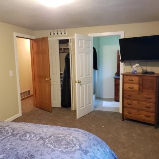A cozy bedroom with a dresser and TV, featuring open doors to a closet and bathroom.