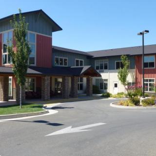 A modern commercial building with a landscaped exterior and a parking lot under clear blue skies.