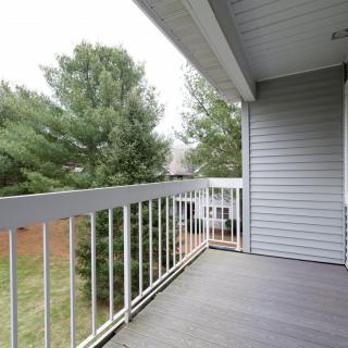A balcony with white railings overlooking a yard with trees.