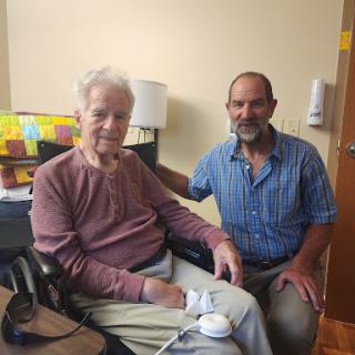 An elderly man shares a moment with his caregiver in a warm indoor setting.