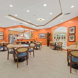 A spacious dining area with orange walls, featuring several tables and chairs under bright lighting.