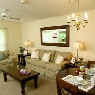 A cozy living room featuring a sofa, coffee table, and dining area with a chandelier.