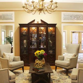 A cozy living room featuring elegant armchairs, a wooden cabinet, and a chandelier overhead.
