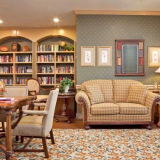 A cozy library room with bookshelves, a sofa, armchairs, and a patterned rug.