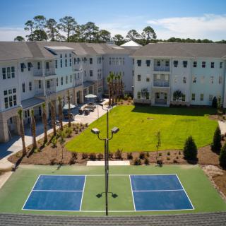 A residential apartment complex with a spacious courtyard, featuring a tennis court and landscaped green areas.