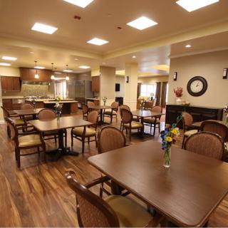A spacious dining area with neatly arranged tables and chairs, featuring a kitchen in the background.
