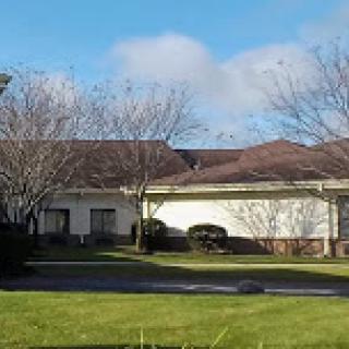 A serene residential building surrounded by trees and a lush green lawn under a clear blue sky.