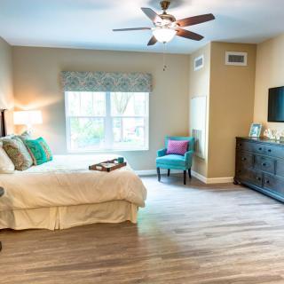 A well-lit bedroom with a comfortable bed, stylish decor, and wooden flooring.