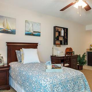 A cozy bedroom with a single bed, nautical artwork, and a ceiling fan.