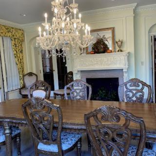 A luxurious dining room featuring an elegant chandelier, a large wooden table, intricately designed chairs, and a classic fireplace.