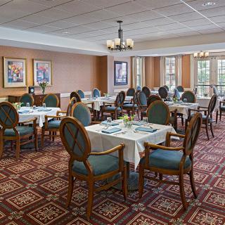 A spacious dining room with elegantly set tables and chairs, featuring a patterned carpet and decorative chandeliers.