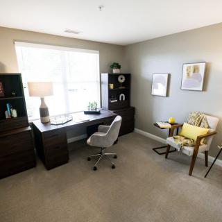 A bright and organized home office featuring a desk, chair, bookshelves, and decor, illuminated by natural light from a large window.