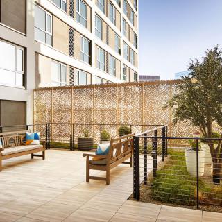 A modern outdoor patio area with wooden benches, greenery, and urban architecture.