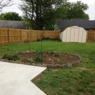 A backyard with a small garden, wooden fence, and storage shed.