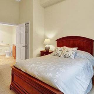 A cozy bedroom with a wooden bed frame, bedside table, and lamp, connected to a bathroom.