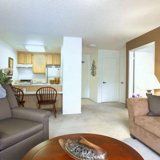 A cozy living room with an open kitchen, featuring comfortable sofas and a wooden table.
