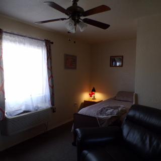A cozy bedroom with a single bed, armchair, and a lit lamp next to the window with curtains.