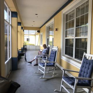 A person sitting on a porch with several rocking chairs.