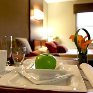 A neatly arranged breakfast tray featuring a green apple and a small bouquet of flowers, set in a cozy hotel room.