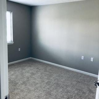 An empty room with gray walls and a carpeted floor, featuring a window.