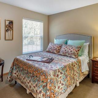 A cozy bedroom with a patterned bedspread and soft pillows, featuring a wooden nightstand and a window letting in natural light.