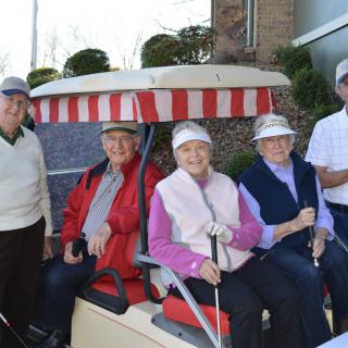 A group of seniors sitting in a golf cart, ready for a round of golf.