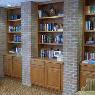 A cozy library corner featuring wooden bookshelves integrated into a brick wall, filled with various books and decorative items.