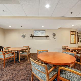 A cozy dining area with round tables and upholstered chairs arranged on a carpeted floor.
