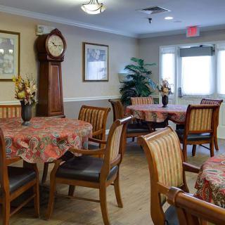 A cozy dining room with decorated tables, wooden chairs, a grandfather clock, and framed wall art.