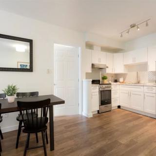 A modern minimalist kitchen with white cabinets and a dining area featuring wood flooring.