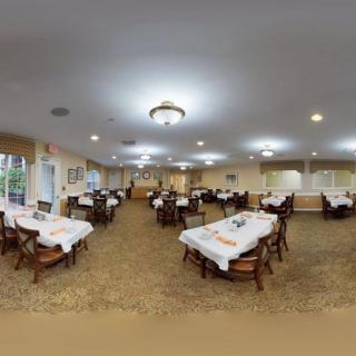 A well-lit dining room with multiple tables set up with white tablecloths.