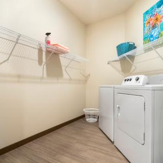 A tidy laundry room featuring a washing machine, dryer, and organized shelves with towels and cleaning supplies.