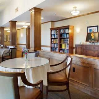 A cozy dining area with round tables, high-backed chairs, and a bookshelf against wood-paneled walls.