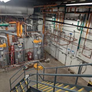 An industrial space showcasing an array of pipes and mechanical equipment, alongside a staircase.