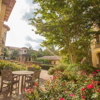 A serene garden patio with tables, chairs, and vibrant flowers under a sunny sky.