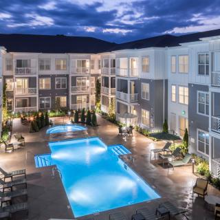 A modern apartment complex with a brightly lit swimming pool at night.
