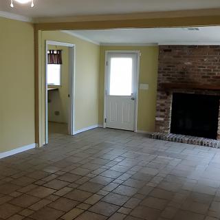 An empty room featuring a brick fireplace and tiled floors, with a door leading to another space.