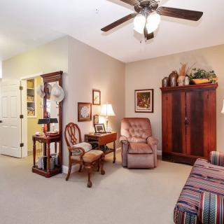 A cozy living room with traditional decor, featuring an armchair, lamp, and ceiling fan.