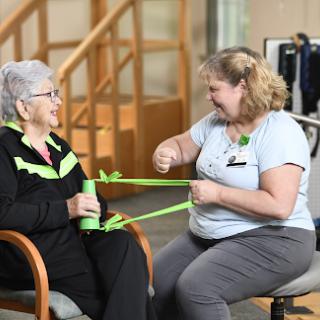 A healthcare professional assists an elderly patient with resistance band exercises during a physiotherapy session.