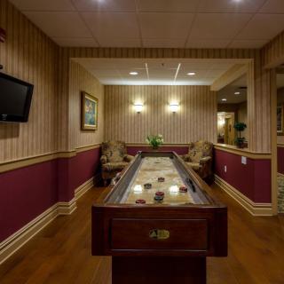 A cozy game room featuring a shuffleboard table, lounge chairs, and a wall-mounted TV.