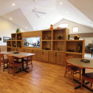 A spacious dining area with wooden tables and chairs, featuring a large shelving unit with a fish tank.