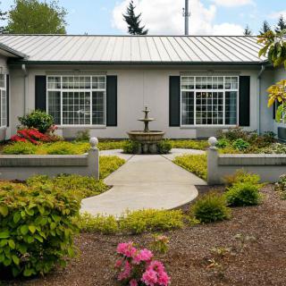 A house with a well-maintained garden, featuring a central fountain and pathway surrounded by shrubs and flowers.