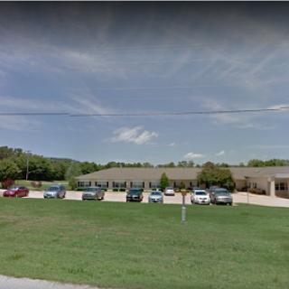 A view of a commercial building with a parking lot filled with vehicles under a partly cloudy sky.